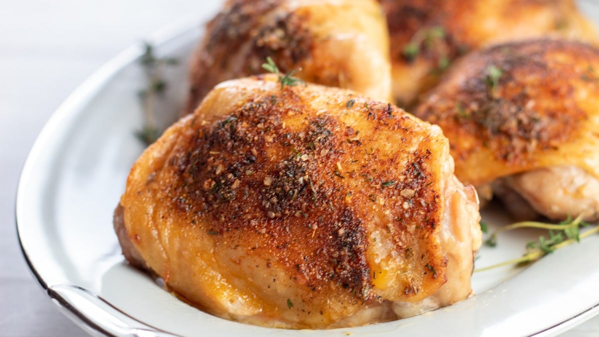 Ampia immagine di cosce di pollo al forno su un piatto da portata bianco.