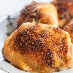 Square close up image of oven baked chicken thighs on a white serving plate.