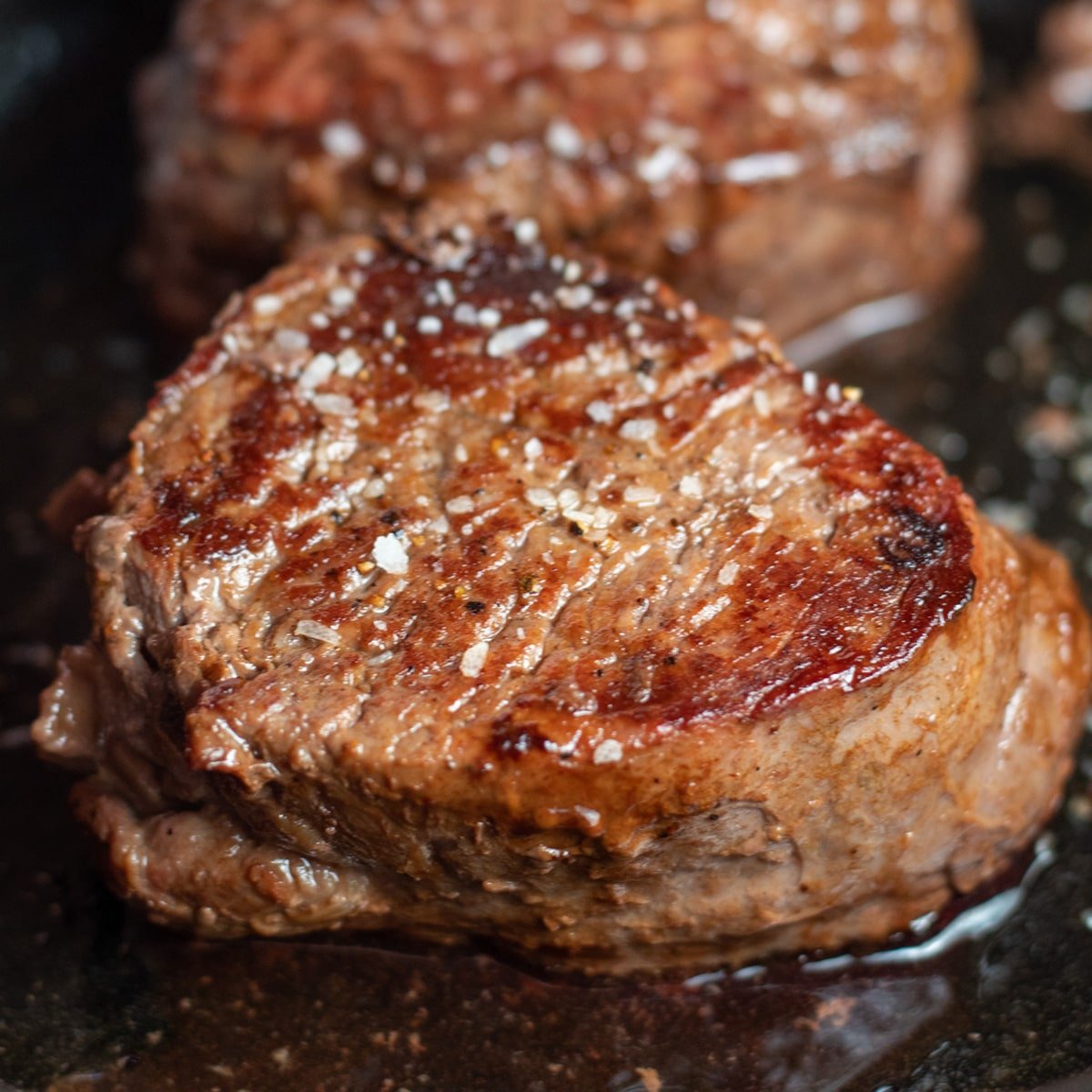 Steak filet mignon pan seared terbaik yang diasinkan dan ditampilkan dalam wajan besi cor.
