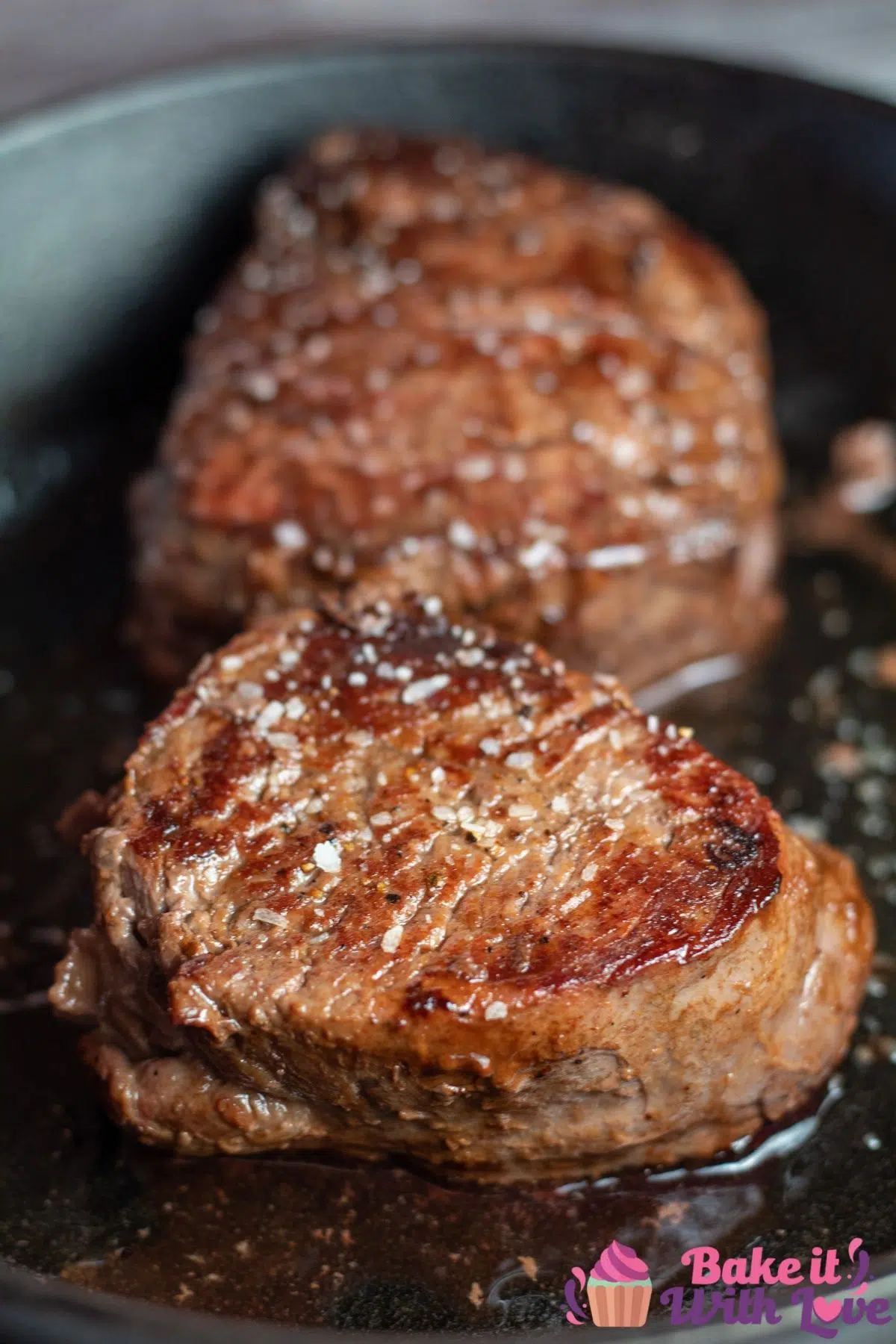 Tall photo of two pan seared filet mignon steaks in cast iron skillet.
