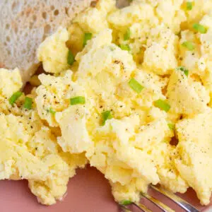 Square close up image of scrambled eggs on rose colored plate with toast on the side.