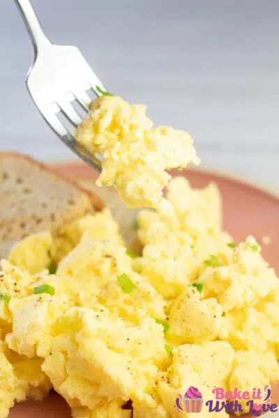 Tall image of scrambled eggs on rose colored plate with toast on the side.