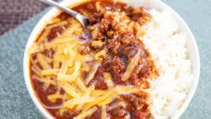 Wide overhead of the dished Texas chili in white bowl with shredded cheddar cheese.