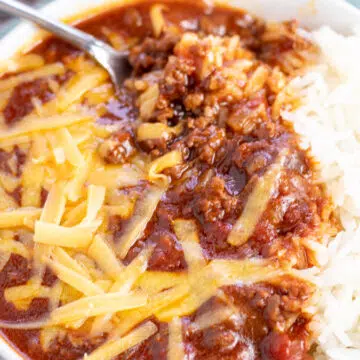 Wide overhead of the dished Texas chili in white bowl with shredded cheddar cheese.