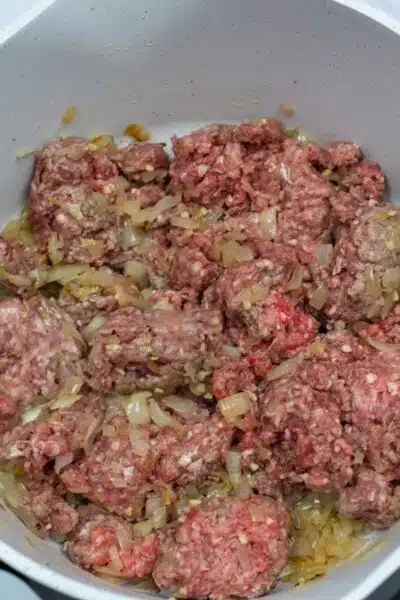 Process photo 3 mix ground beef with sauteed onion and garlic as it cooks.