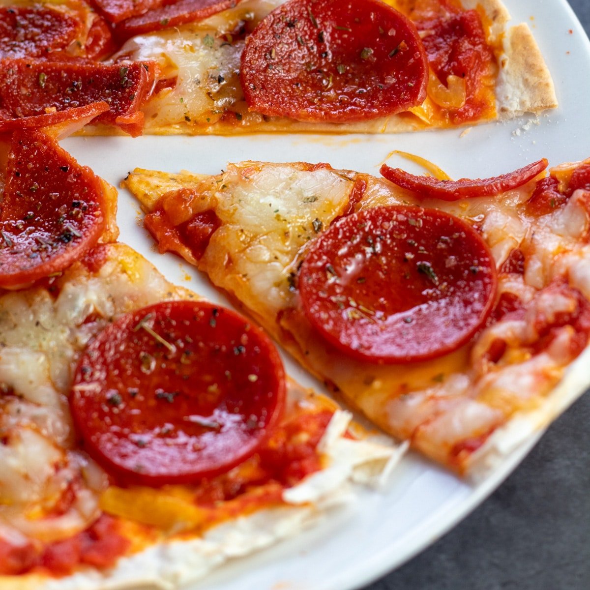Sliced pepperoni tortilla pizza on white plate.
