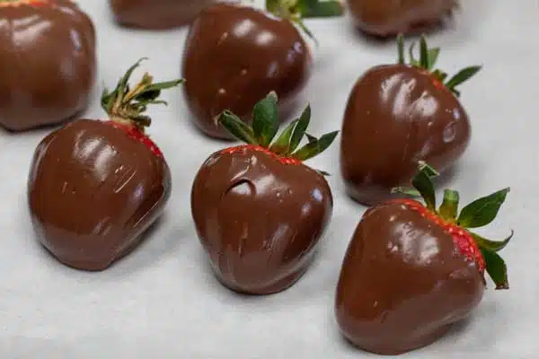 Chocolate dipped strawberries sitting on a baking sheet setting up.