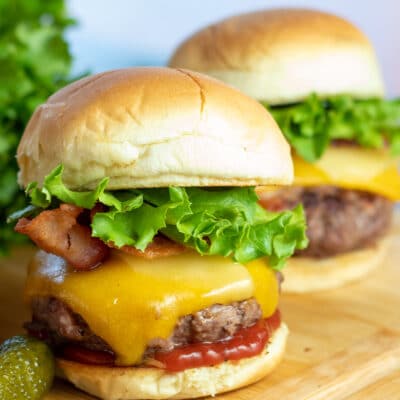 Juicy, tasty venison burgers on soft buns with cheese, bacon, lettuce, and condiments.
