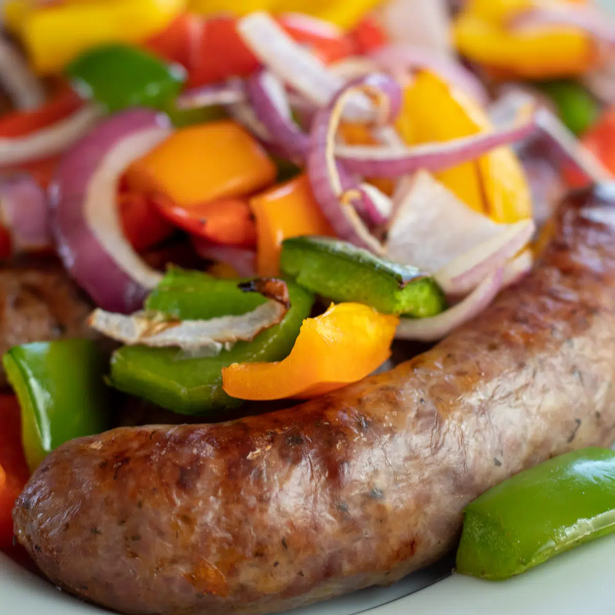 Square close up image of sausage and peppers on a white plate.