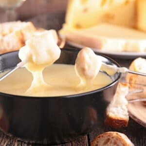Gesmolten cheddar zwitserse kaas findue in zwarte pot met brood ondergedompeld in om te eten.