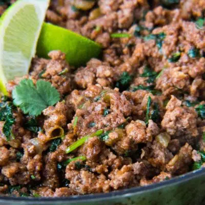 Tall image of taco meat in a cast iron pan with a lime wedge.