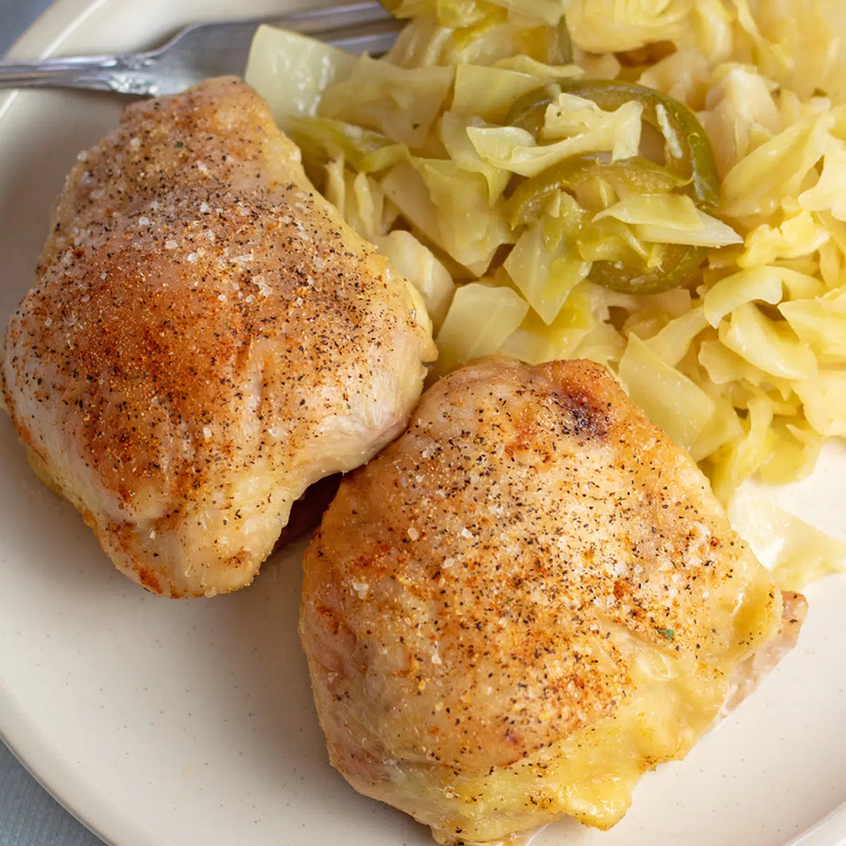 Best air fryer chicken thighs angled overhead view with fried cabbage and jalapenos on white plate.