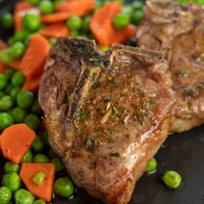 Pin image with text divider of air fryer lamb chops on a black plate with peas and carrots on the side.