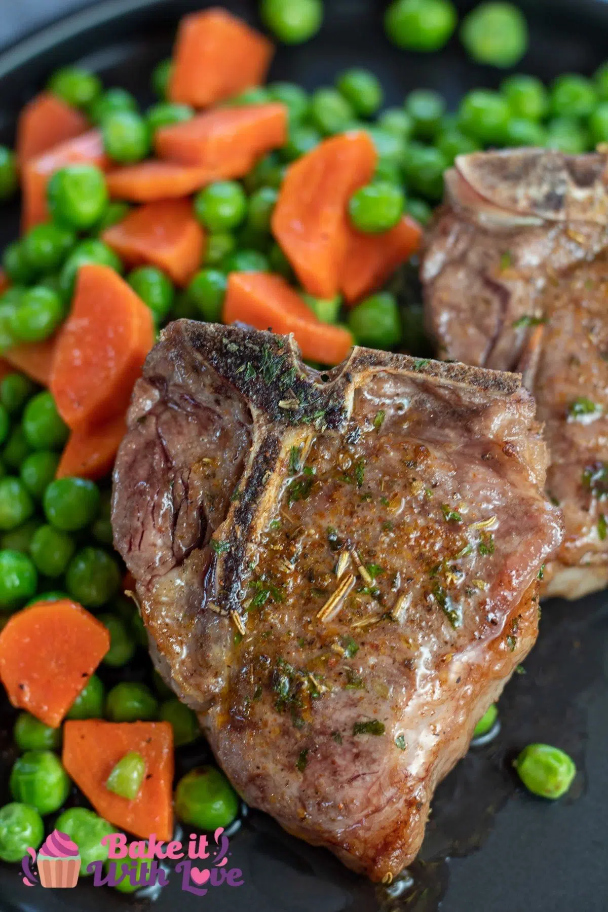Tall image of air fryer lamb chops on a black plate with peas and carrots on the side.