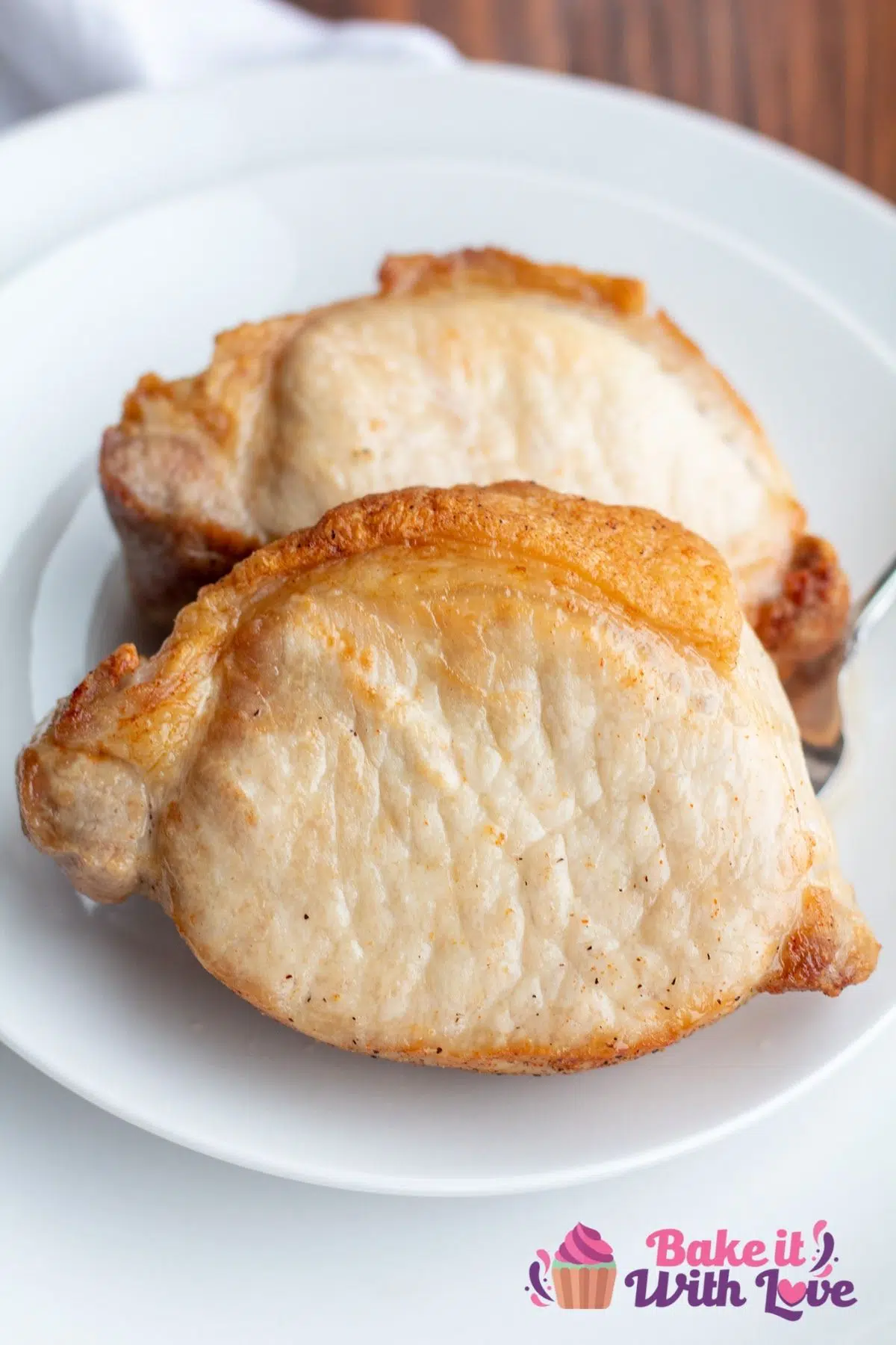 Two tasty air fryer pork loin chops on white plate with wooden background.