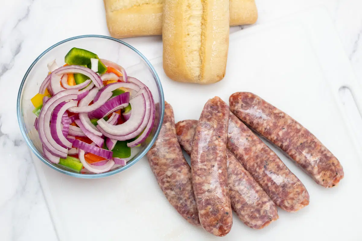 Air fryer sausage and peppers and onions ingredients with optional buns on the side for serving.