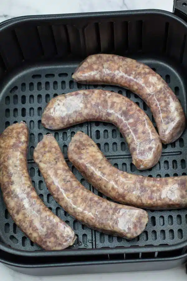 Process photo 1 raw sausage links in the air fryer basket with space for air to circulate.