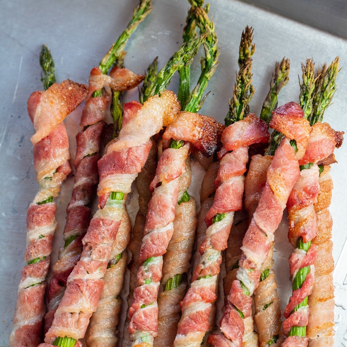 Delicious baked bacon wrapped asparagus spears on metal tray.