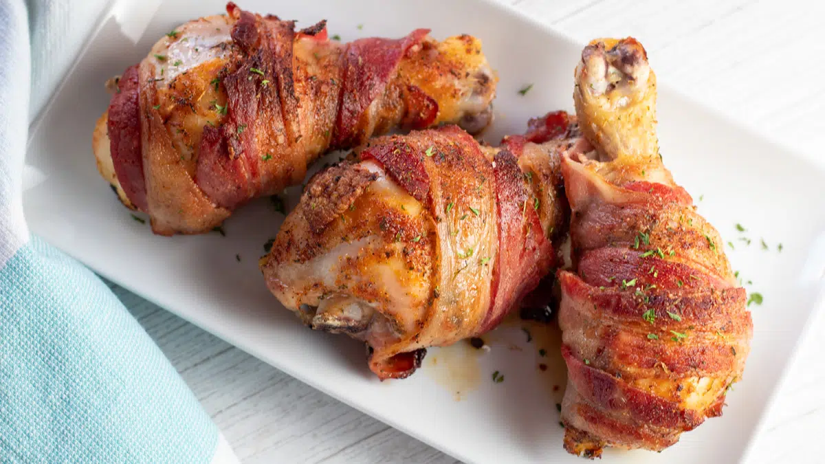 Overhead view of the tasty bacon wrapped baked chicken drumsticks on white plate.