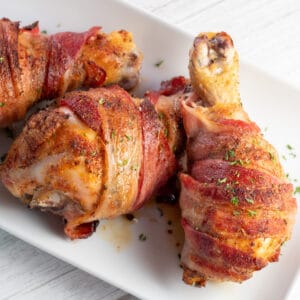 Los mejores muslos de pollo al horno envueltos en tocino servidos en un plato blanco.