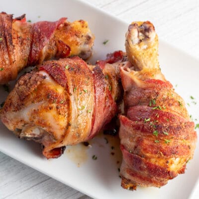 Best bacon wrapped baked chicken drumsticks served on white plate.