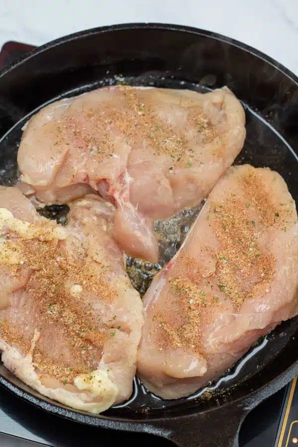 Process photo 3 showing seasoned chicken breasts in cast iron pan cooking.