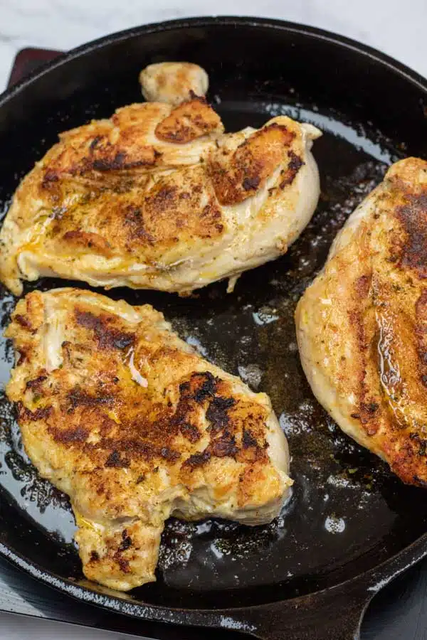 Process photo 4 showing seasoned chicken breasts in cast iron pan cooking opposite side.