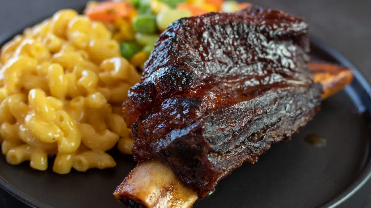 Wide image of baked bbq short ribs plated with mac and cheese.