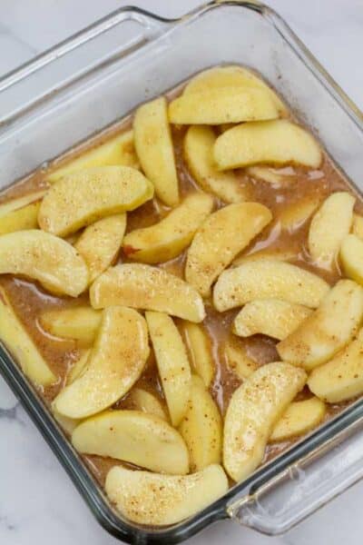 Process photo 5 showing sliced apples with cinnamon mixture in baking dish.