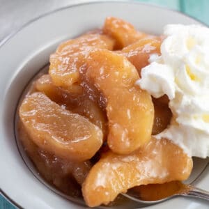 Square image of baked cinnamon apples in a bowl with whipped cream.