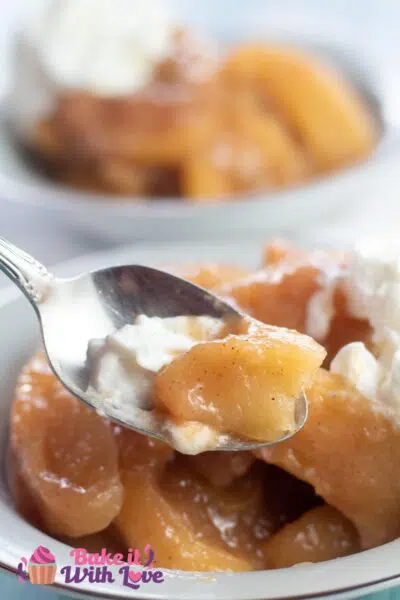 Tall image of baked cinnamon apples in a bowl with spoon.
