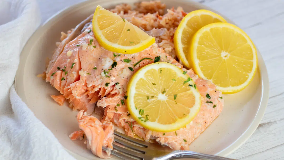 Overhead of the plated baked steelhead trout with lemon slices and garlic butter sauce.