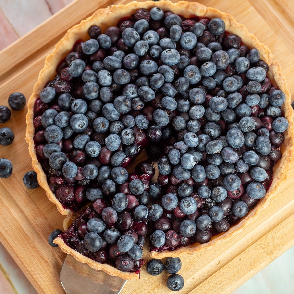 Gambar persegi kue tar blueberry di atas talenan dengan potongan yang dibuang.