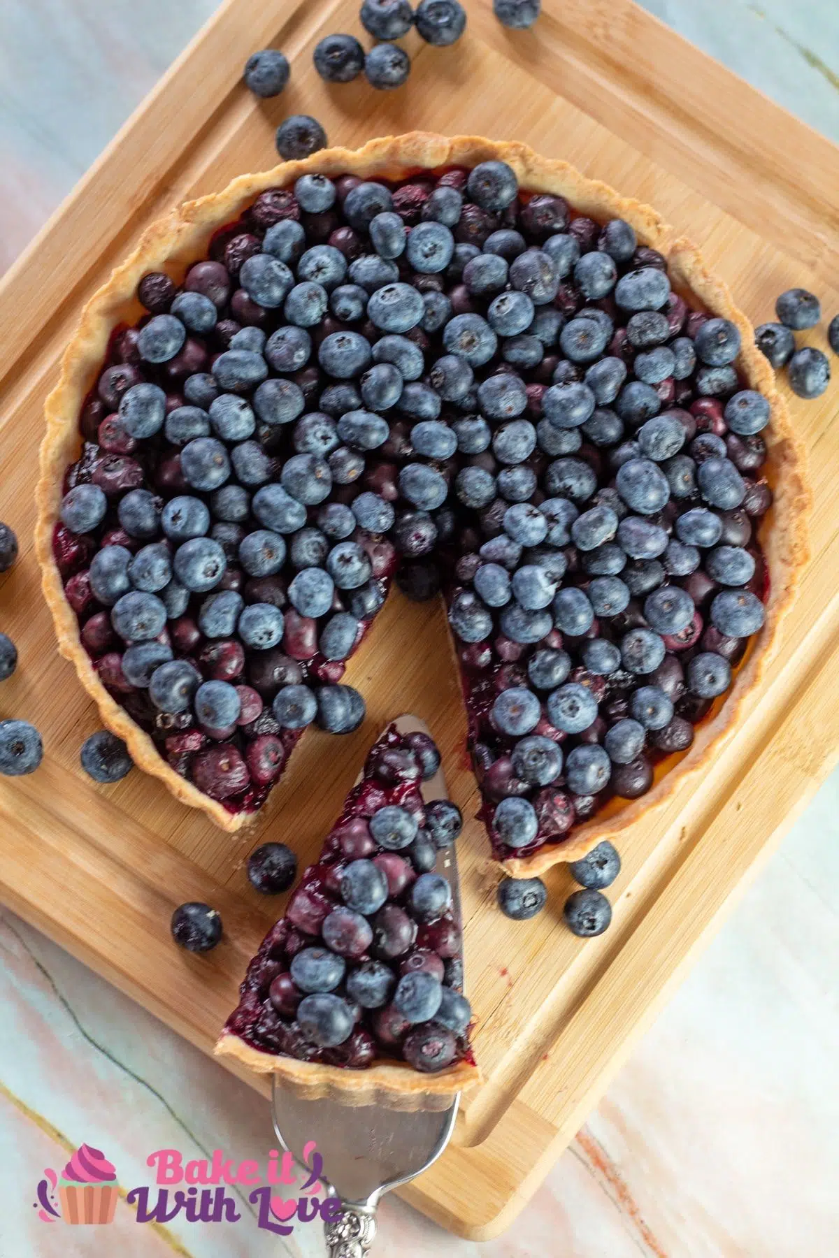 Tall image of blueberry tart on a cutting board with a slice pulled out.
