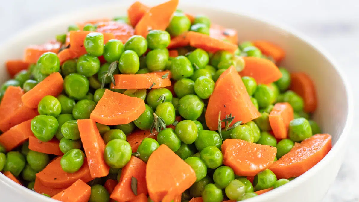 Wide image of a white bowl filled with peas and carrots.