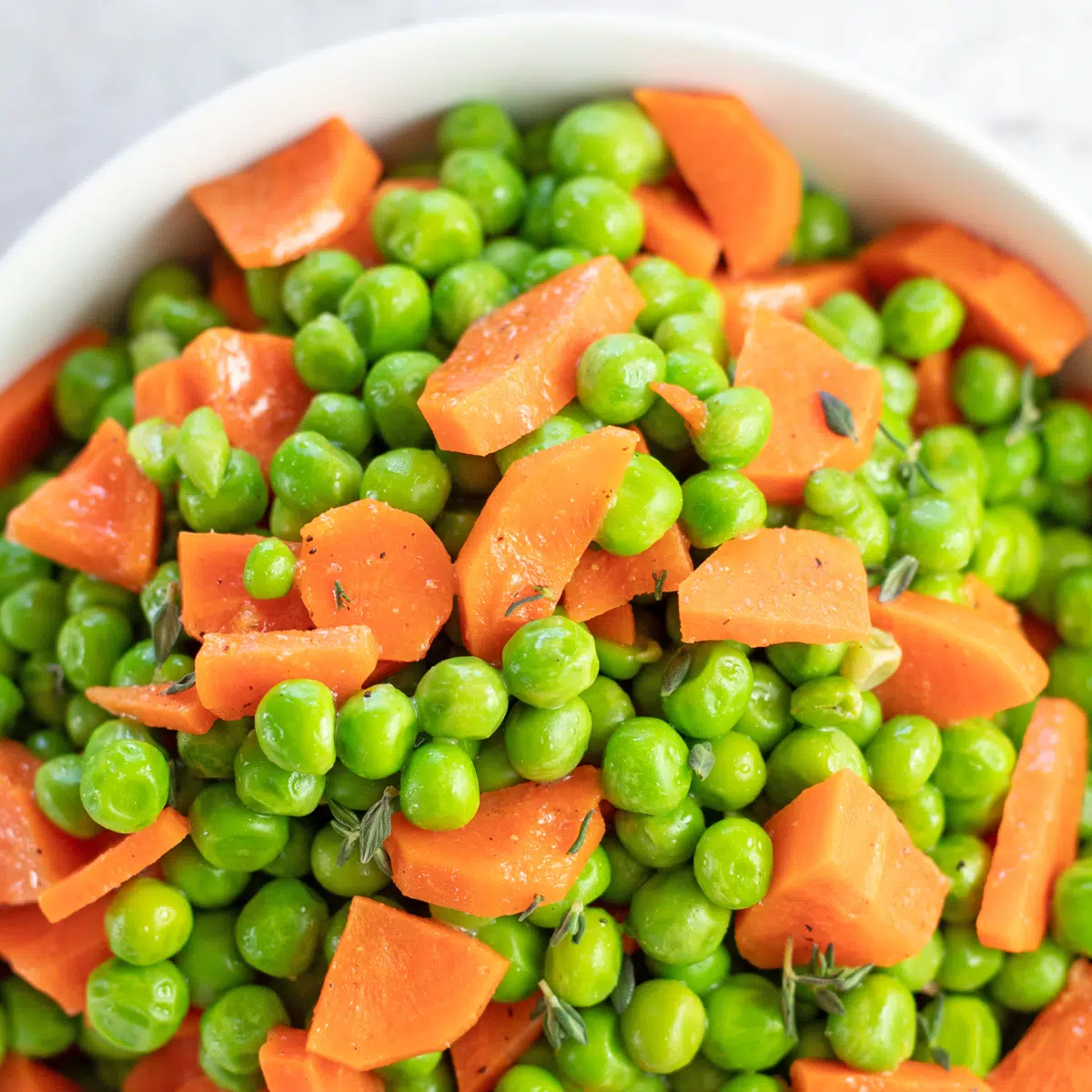 Square image of a white bowl filled with peas and carrots.