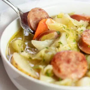 Perfectly tasty cabbage soup with kielbasa and potatoes in white bowl.