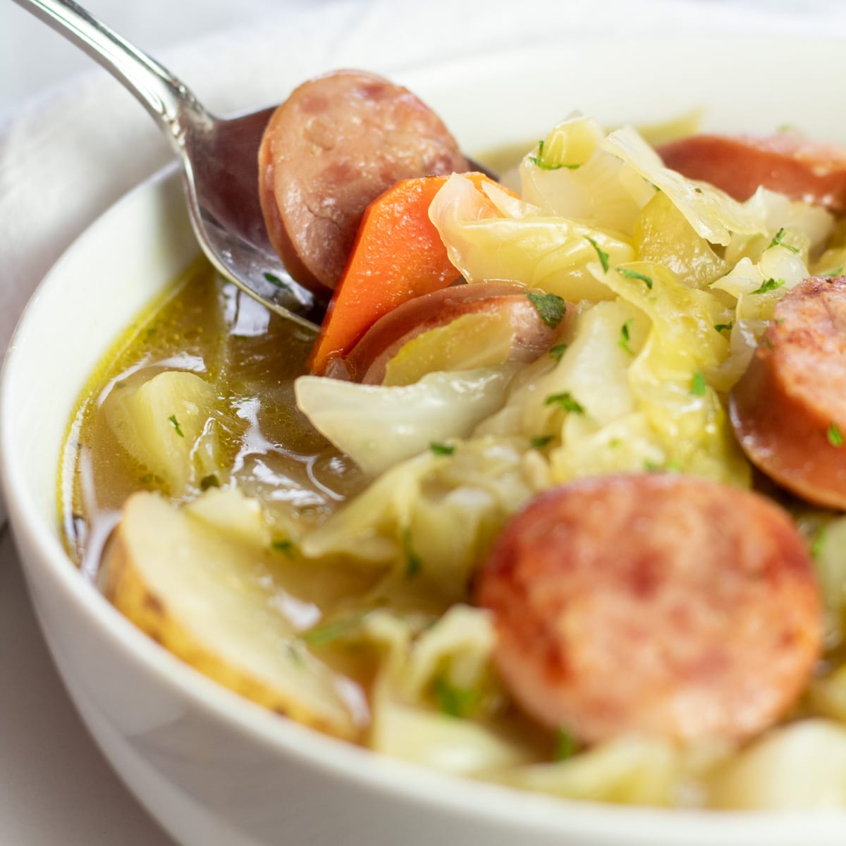 Sopa de repolho perfeitamente saborosa com kielbasa e batatas em tigela branca.