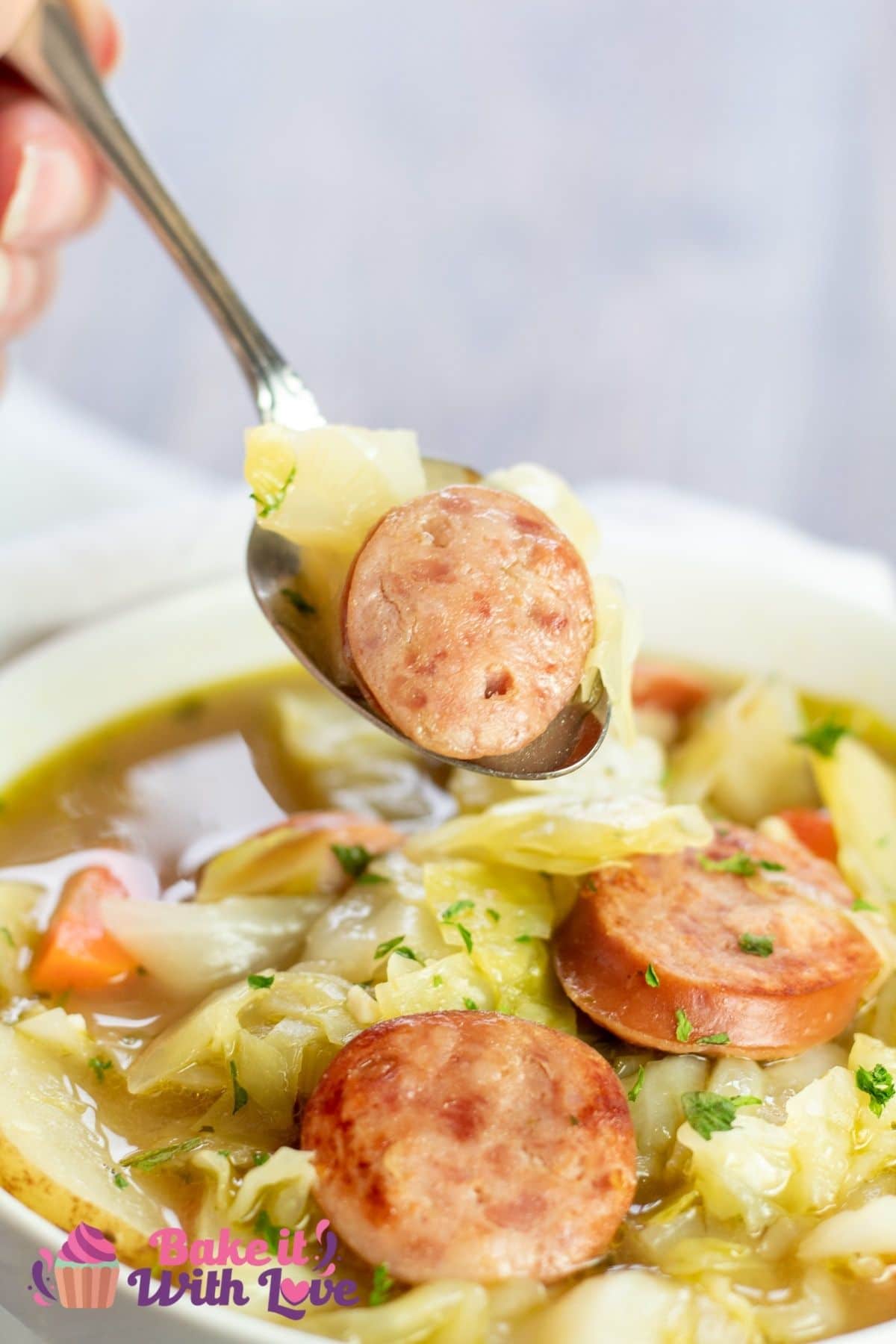 Tall image of the cabbage soup with kielbasa being spooned from bowl.