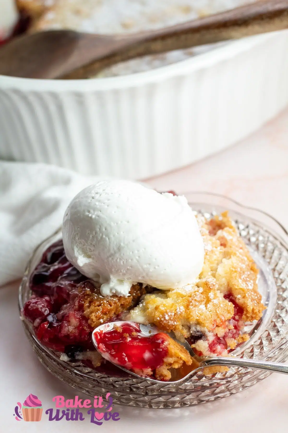 Tall image of the cherry blueberry dump cake served on plate with scoop of vanilla ice cream.