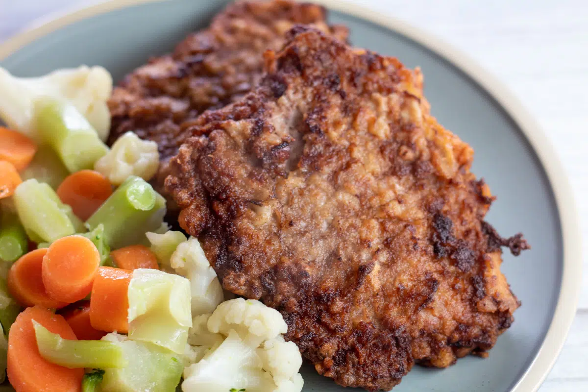 Wide image of chicken fried cube steak on a plate with vegetables.