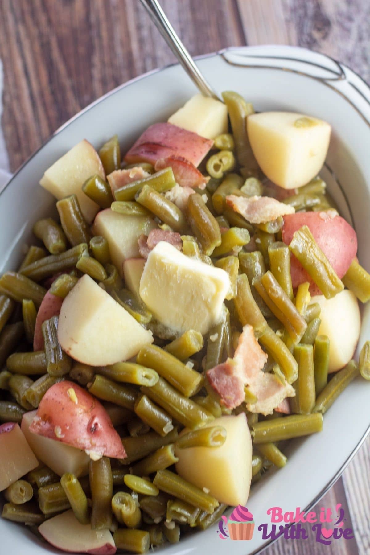 Tall image of crockpot green beans and potatoes in a white serving dish.