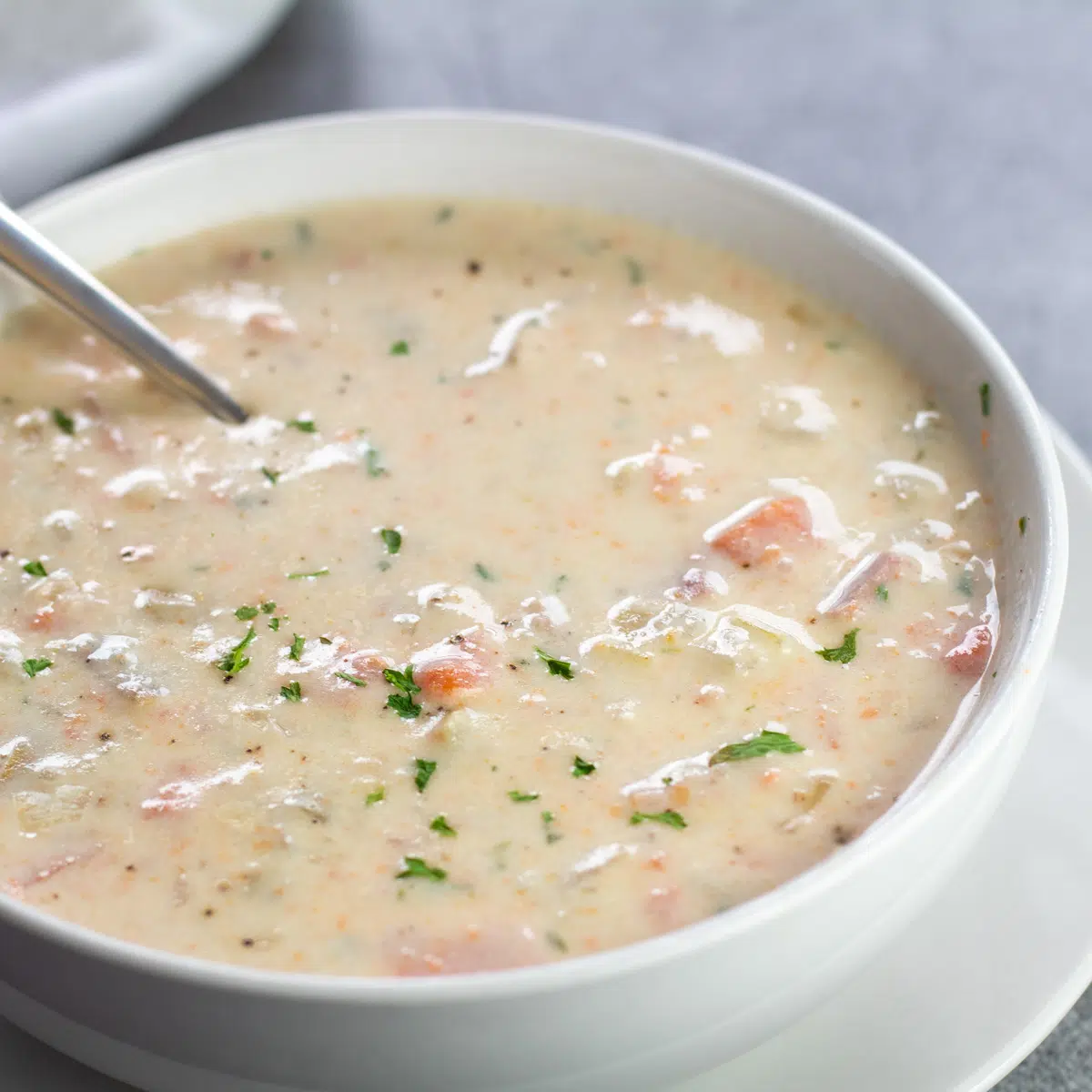Sup kentang ham krim crockpot yang lezat dalam mangkuk putih dengan sendok.