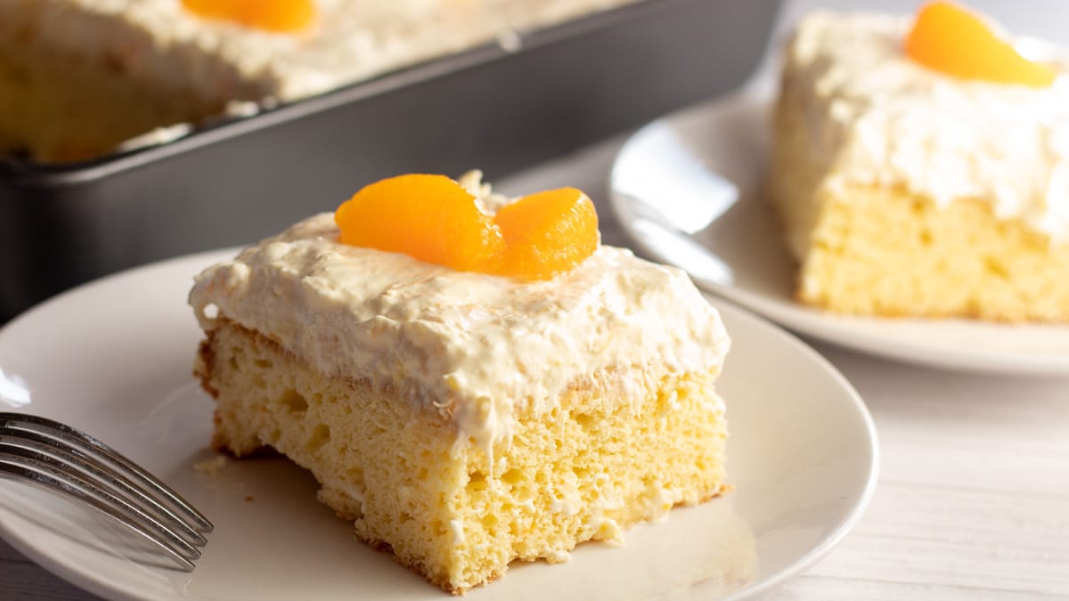 Широко изображение на парче торта с мандарина и портокал върху бяла чиния.