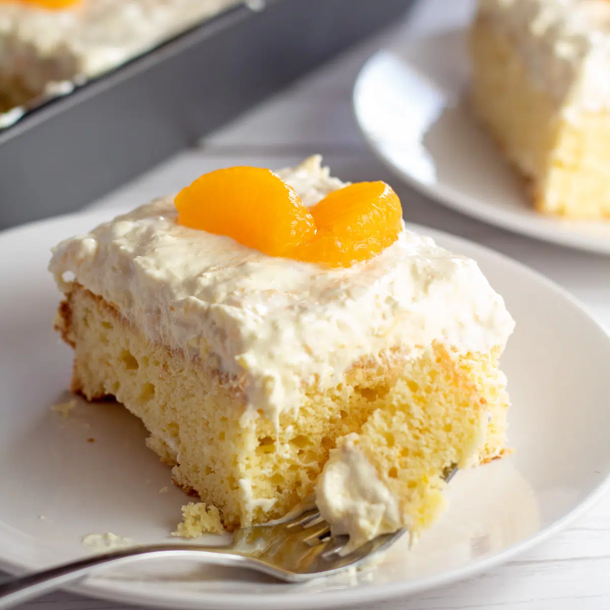 Square image of mandarin orange cake slice on a white plate.