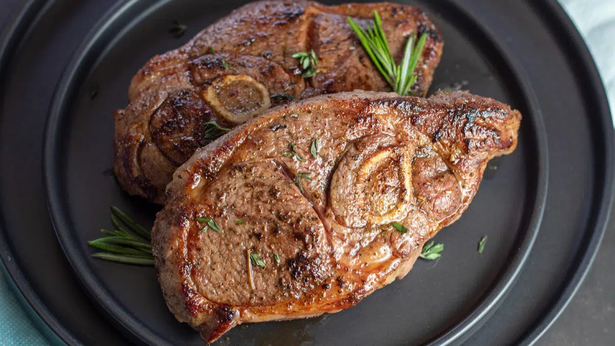 Wide overhead of the pair of pan seared lamb shoulder chops on set of black plates.