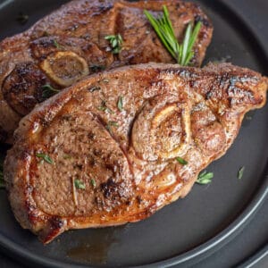 Closeup on the best pan seared lamb shoulder chops with rosemary garnish on black plate.