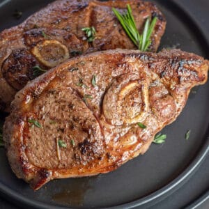 Primer plano de las mejores chuletas de cordero a la plancha con guarnición de romero en un plato negro.