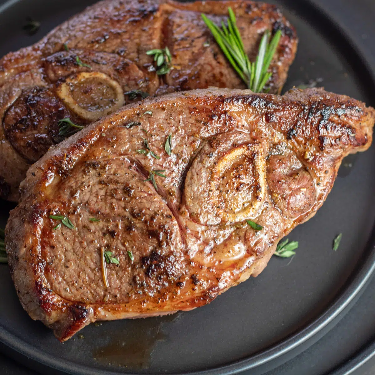 Closeup pada daging bahu domba panggang terbaik dengan hiasan rosemary di piring hitam.