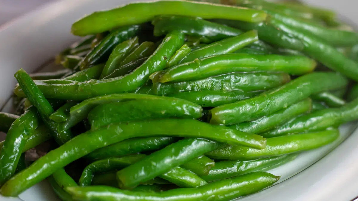 Wide image of sauteed green beans in a serving dish.